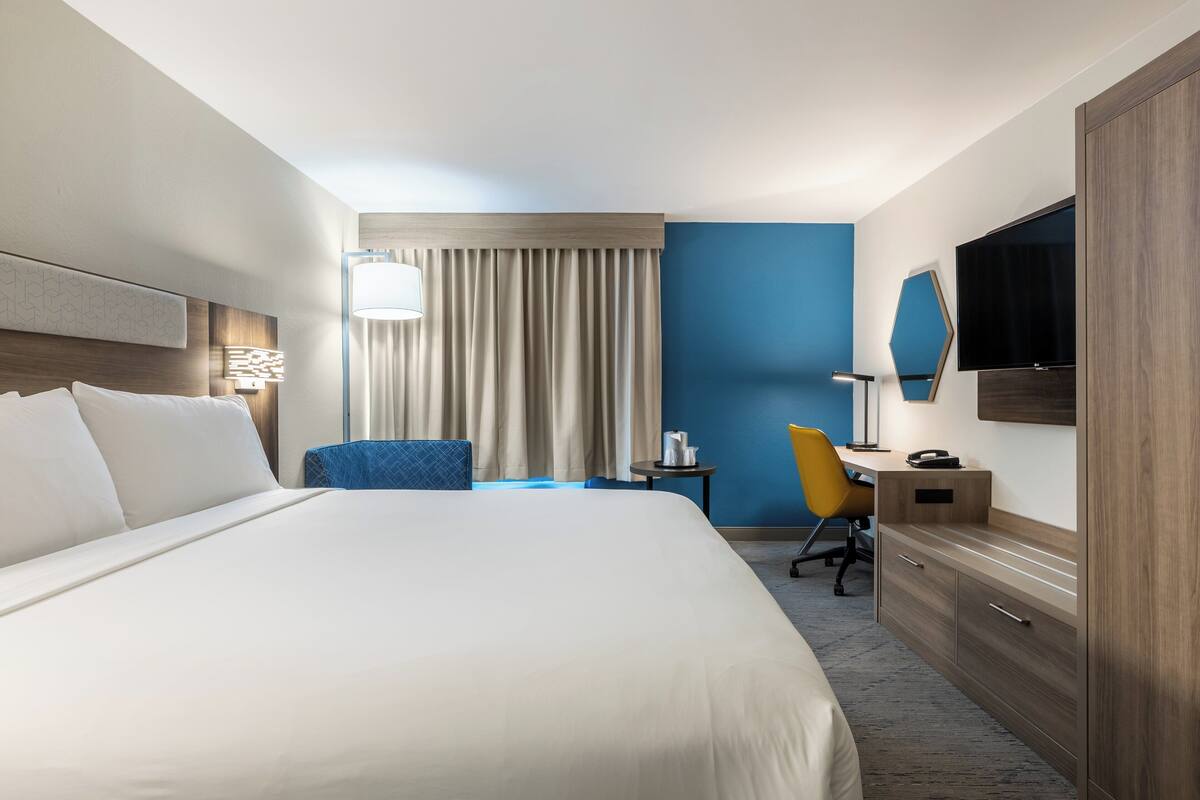 Une chambre d’hôtel avec un grand lit, un bureau, une chaise, une télévision et une armoire.