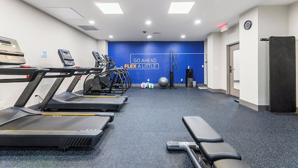 Une salle de sport équipée de tapis de course, d’un banc et de ballons d’exercice.