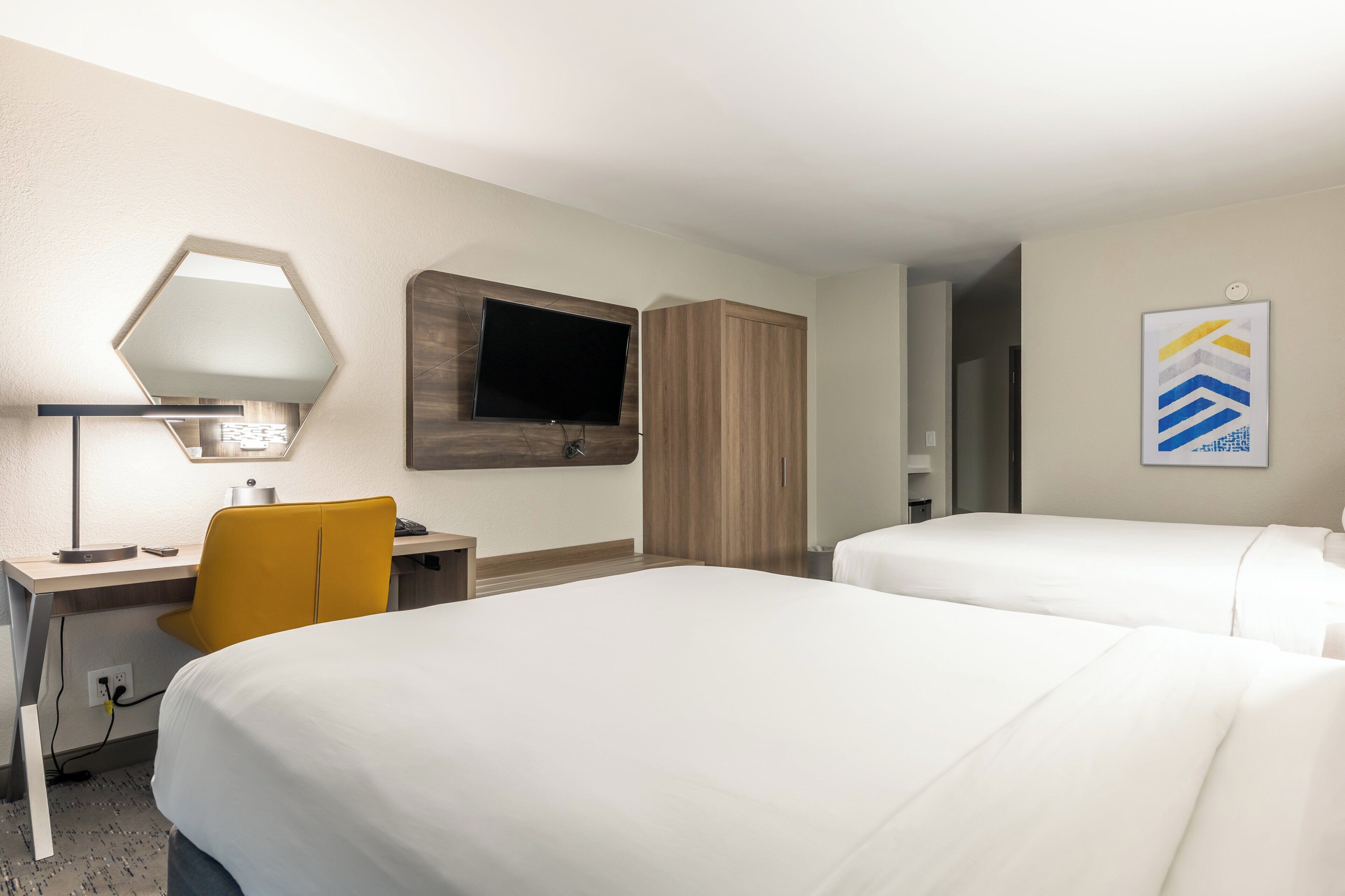 Habitación de hotel con dos camas, un escritorio con silla, un televisor montado en la pared y un armario.
