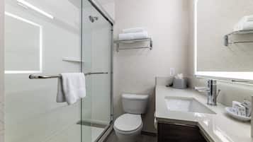 Un baño moderno con cabina de ducha de vidrio, inodoro blanco, lavabo con espejo y toallero.