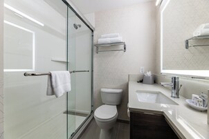 Ein modernes Badezimmer mit Duschkabine aus Glas, einer weißen Toilette, einem Waschbecken mit Spiegel und einem Handtuchhalter.