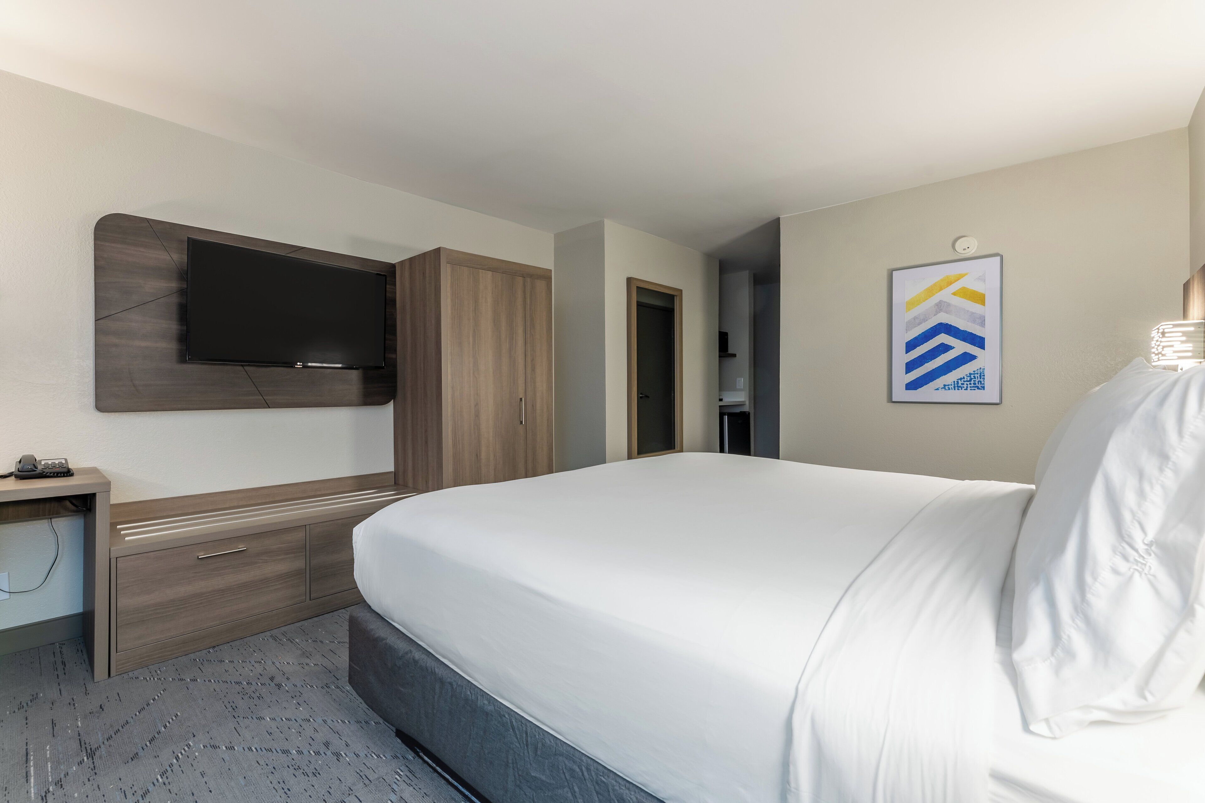 Une chambre d’hôtel dotée d’un grand lit, d’un téléviseur à écran plat fixé au mur, d’une armoire en bois et d’un petit bureau avec un téléphone.