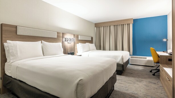 A hotel room with two beds, a desk, a chair, and a large window with curtains.