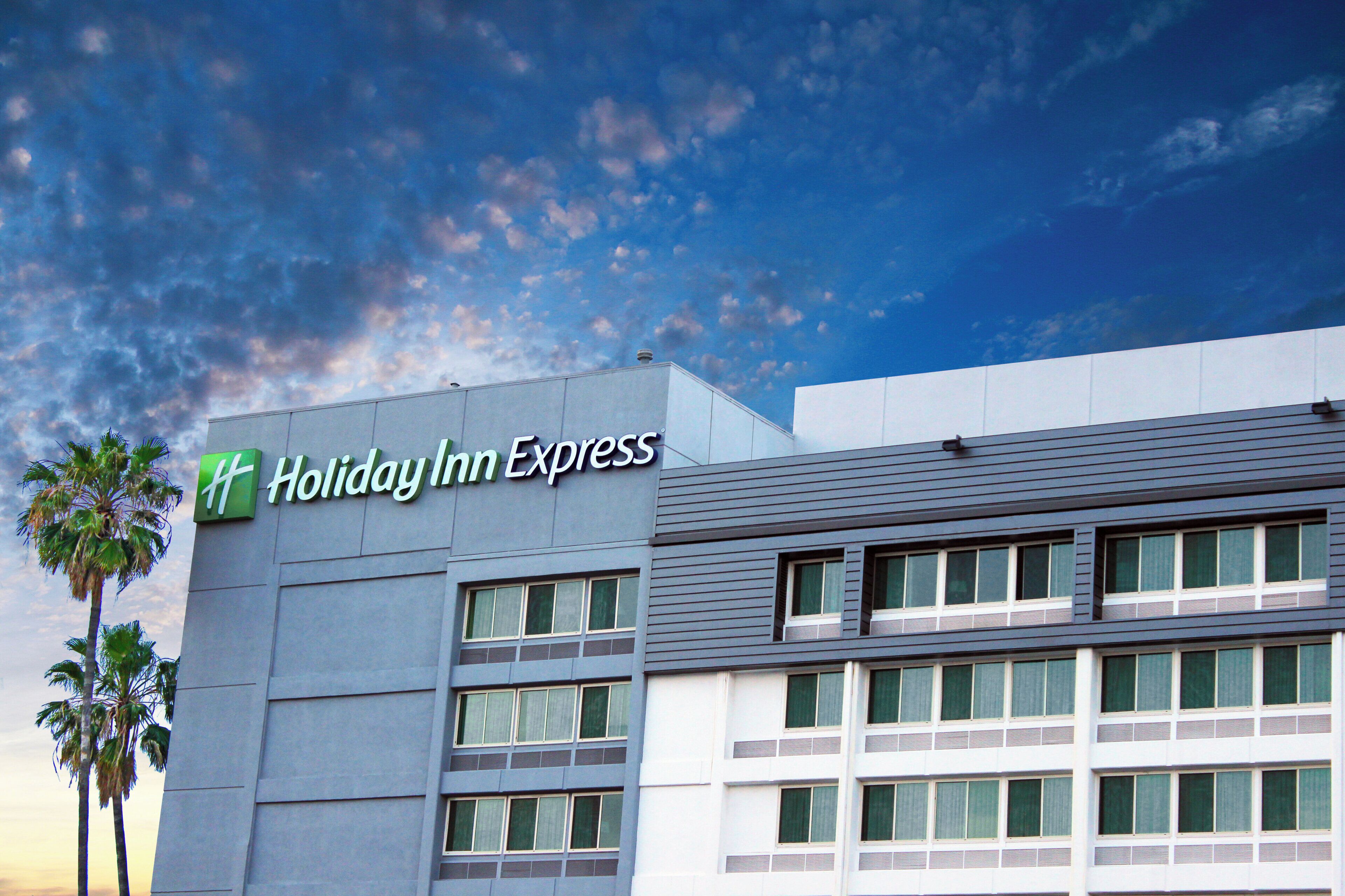 Edificio Holiday Inn Express con fachada moderna, amplias ventanas y cielo despejado al fondo.