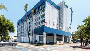 A modern hotel with a blue and white facade, multiple floors, and American flags displayed. - Holiday Inn Express Van Nuys by IHG (Van Nuys)