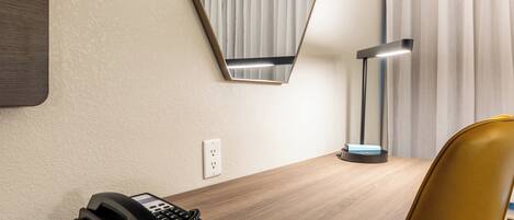 Habitación de hotel con un escritorio de madera, un teléfono, un espejo, una lámpara y una silla.