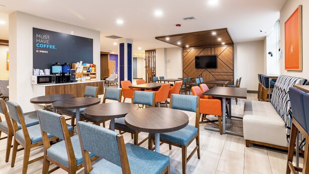 A modern cafe with round tables and blue chairs, a coffee station, and a TV on the wall. - Holiday Inn Express Van Nuys by IHG (Van Nuys)