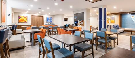 A modern hotel lobby with multiple seating areas, including tables and chairs, and a large screen displaying a map.