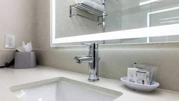 A modern bathroom with a large mirror, chrome faucet, and a bowl containing toiletries.
