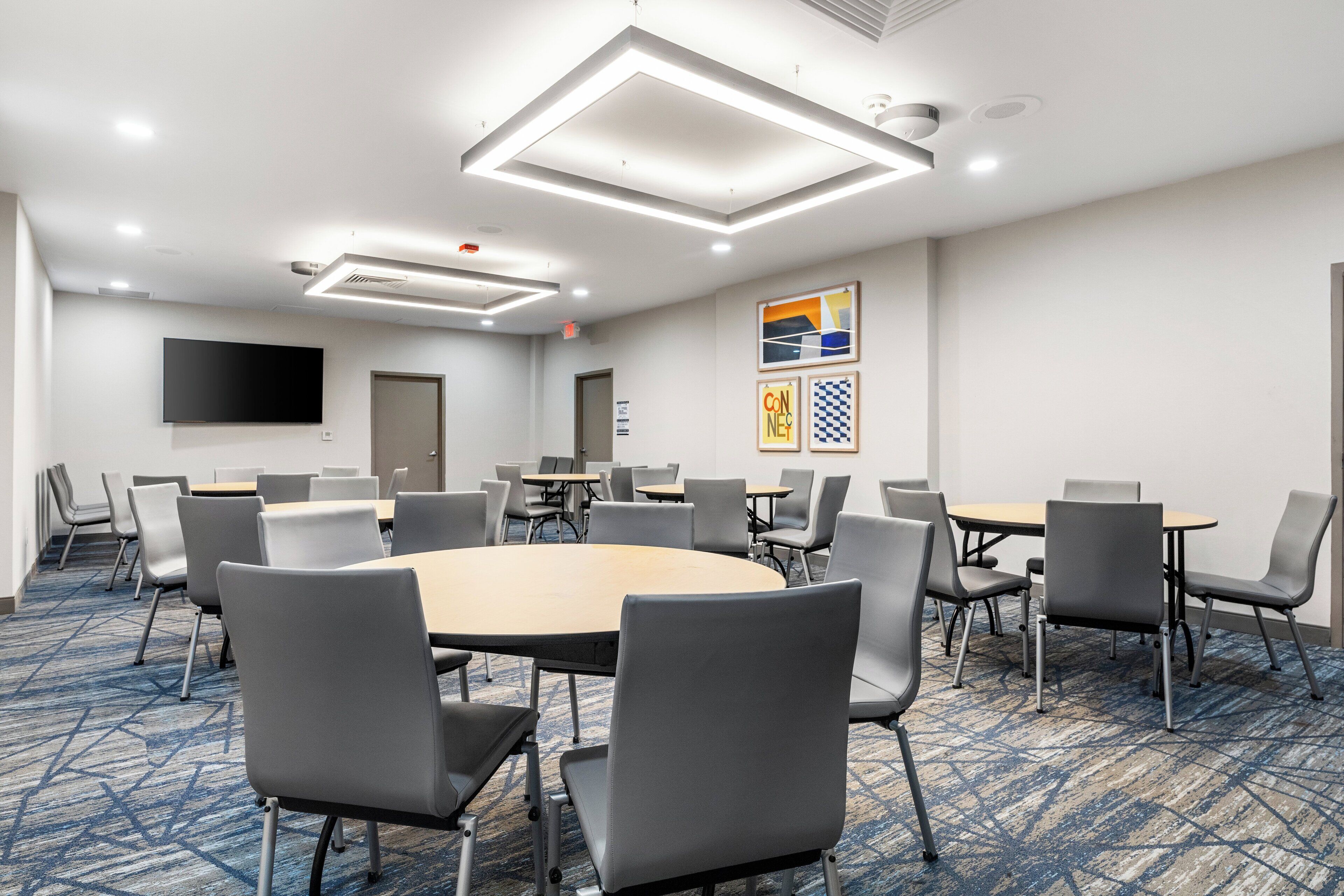 A conference room with a round table, gray chairs, and a flat-screen TV on the wall.