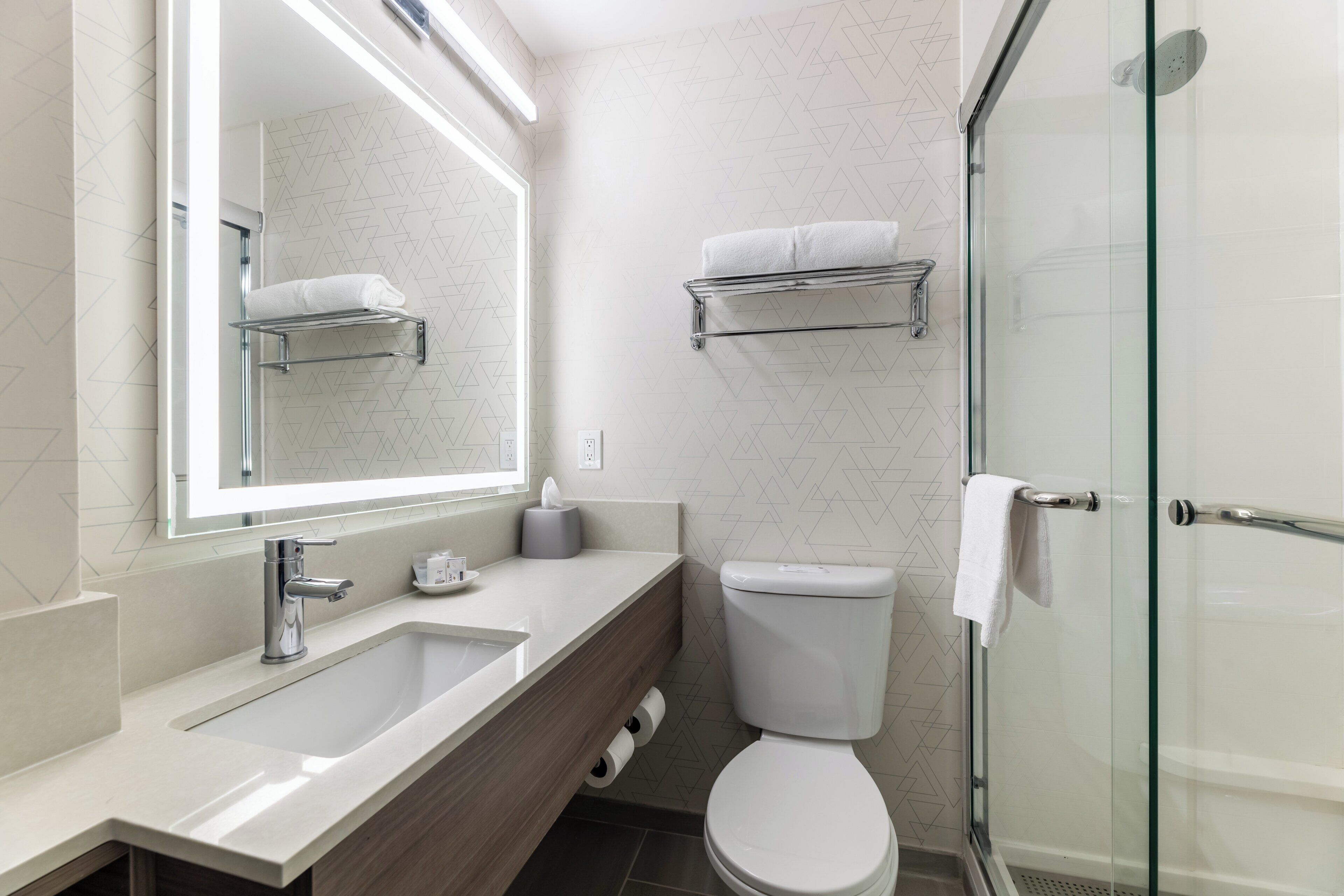 A modern bathroom with a sink, mirror, toilet, and glass shower enclosure.
