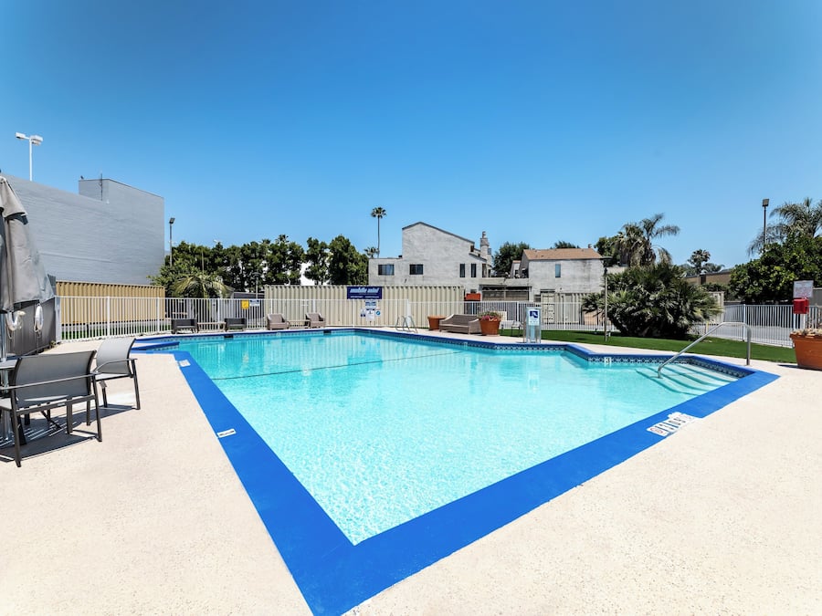 A rectangular pool with a blue edge, surrounded by a white deck. There are lounge chairs and a table with umbrellas.