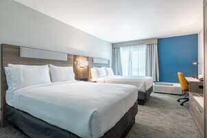 Ein Hotelzimmer mit zwei Betten, einem Schreibtisch, einem Stuhl und einem großen Fenster mit Vorhängen.