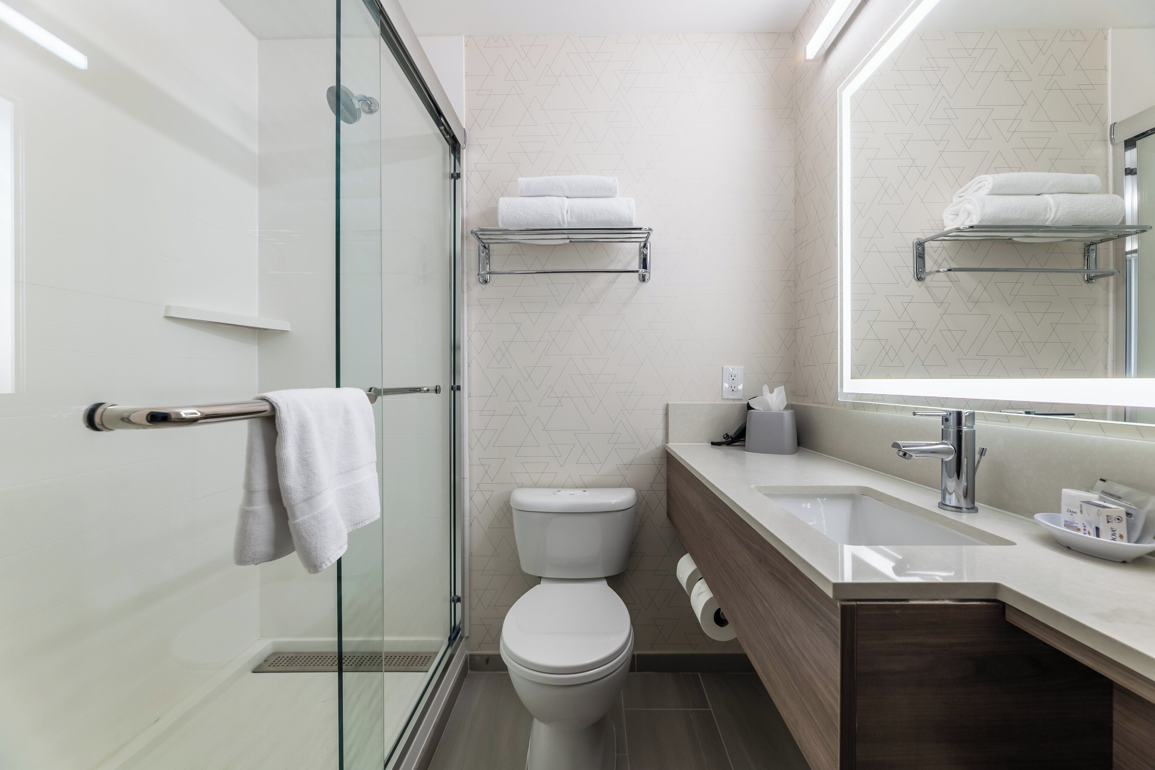 A modern bathroom with a glass shower enclosure, a white toilet, a vanity with a mirror, and a towel rack.