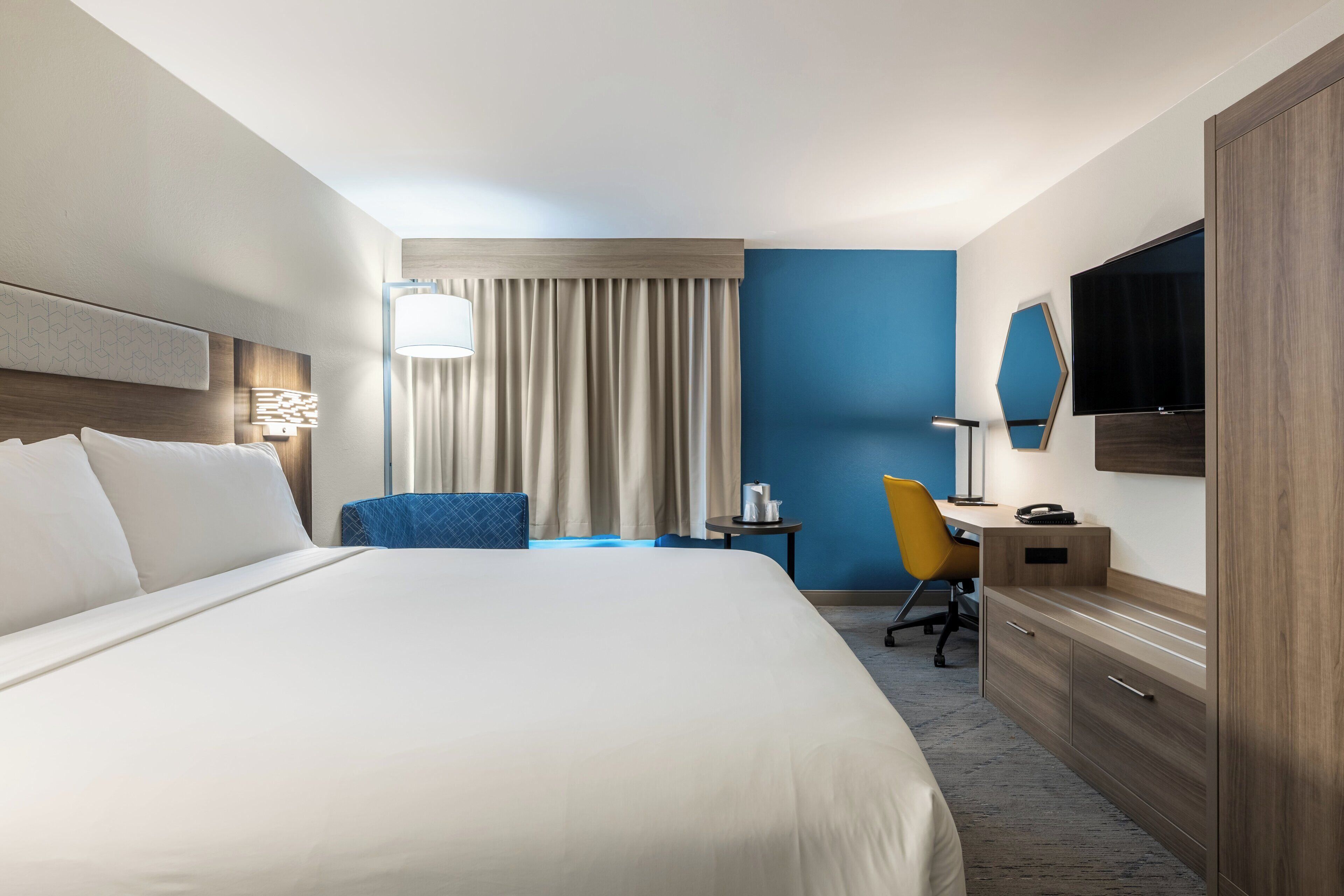 Une chambre d’hôtel avec un grand lit, un bureau, une chaise, une télévision et une armoire.