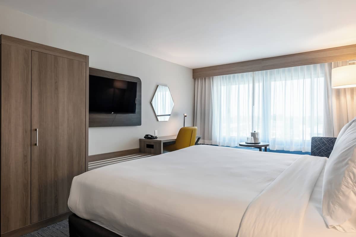 Habitación de hotel con una cama grande, un escritorio con silla, un televisor y una ventana con cortinas.