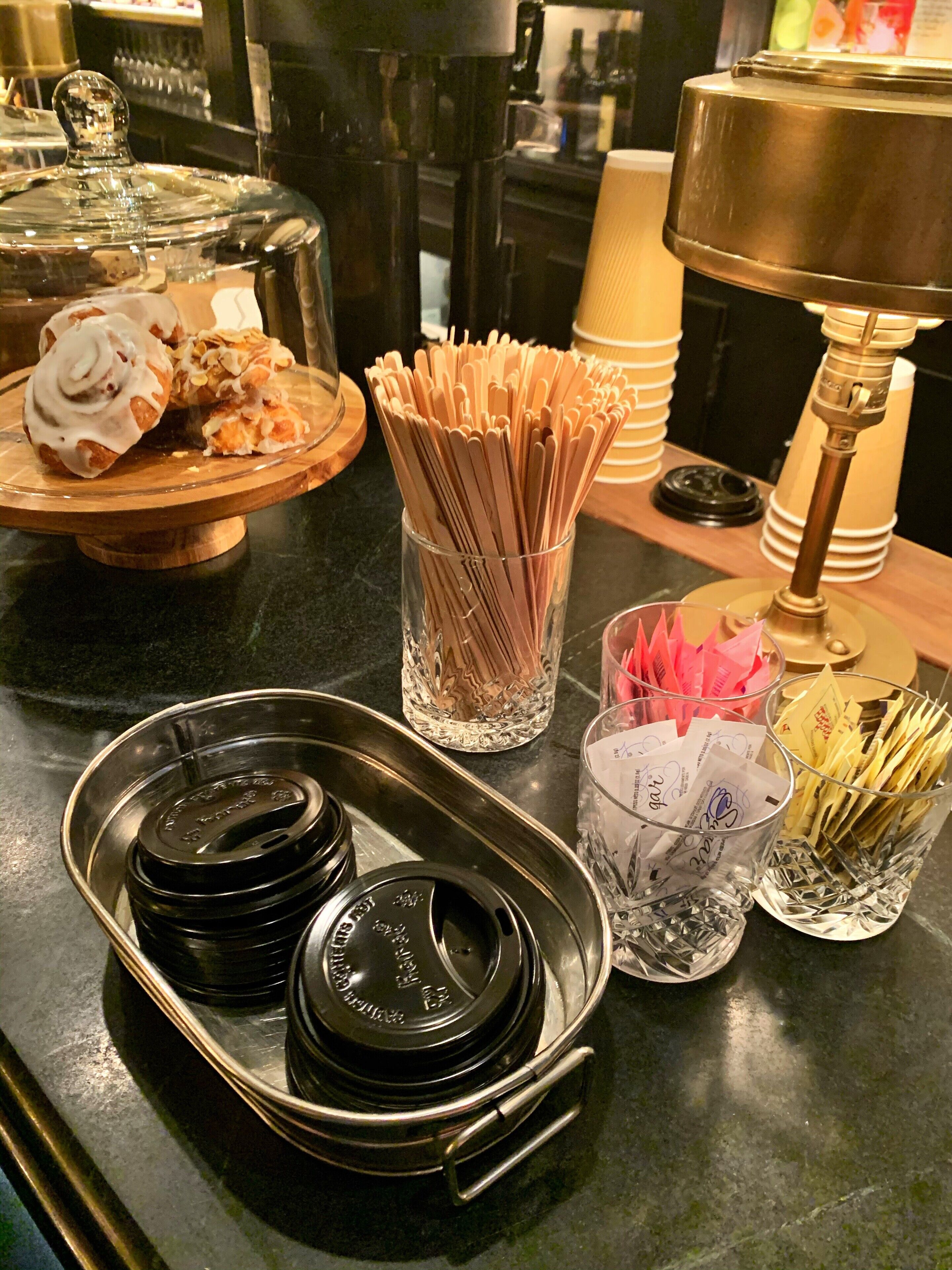 A kitchen counter with various items including a glass jar with utensils, a tray with black lids, and a glass with papers.