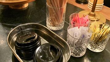 A kitchen counter with various items including a glass jar with utensils, a tray with black lids, and a glass with papers.