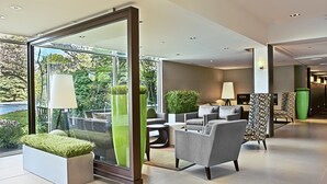 A modern lobby with a glass partition, seating area, and indoor plants. - Weber's Hotel & Restaurant (Ann Arbor)