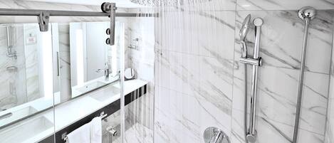 A modern bathroom with a glass-enclosed shower, a handheld showerhead, and a wall-mounted faucet.