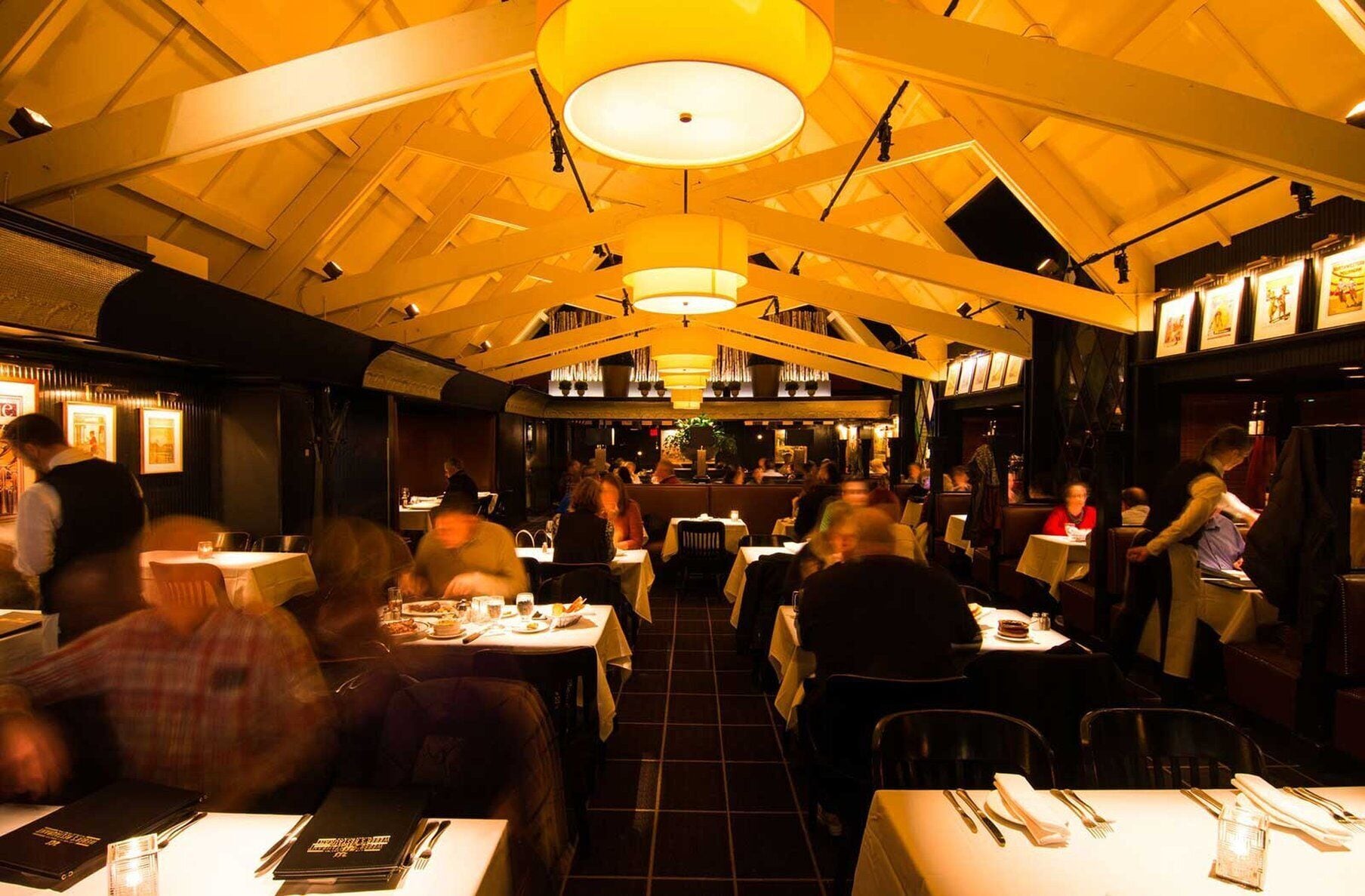 Restaurante com pé direito alto e iluminação acolhedora, com mesas e cadeiras dispostas para refeições.