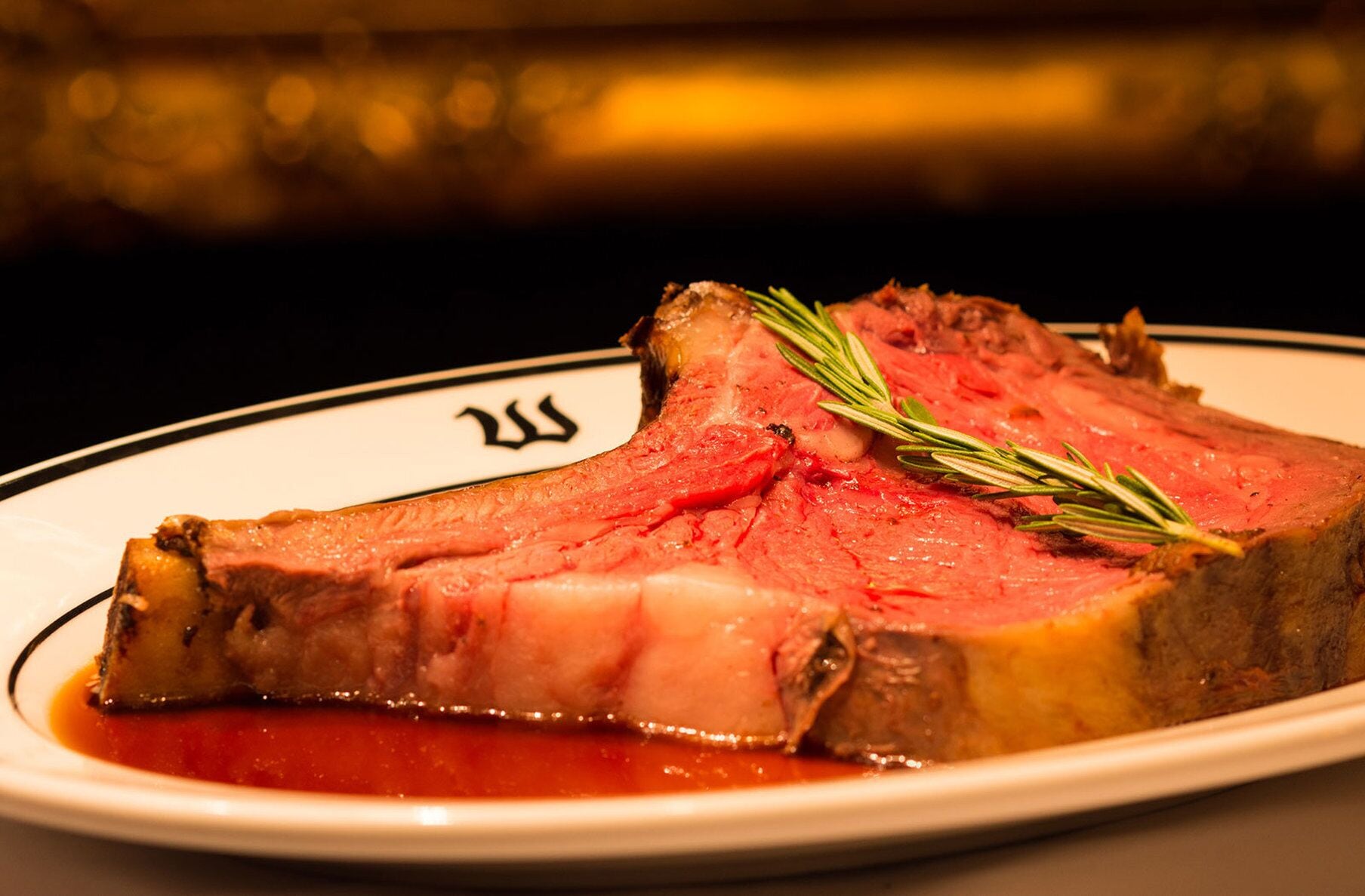 Une assiette de tranches de bœuf rôti, garnie d’une branche de romarin, servie dans une assiette blanche à bordure noire.