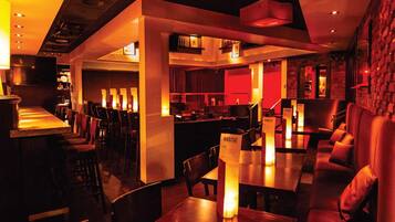 Un restaurante con una decoración moderna, que incluye una zona de bar, mesas y sillas, e iluminación ambiental cálida.