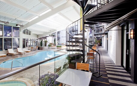 A spacious indoor pool area with a spiral staircase, lounge chairs, and a dining area with tables and chairs.