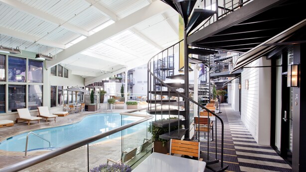 A spacious indoor pool area with a spiral staircase, lounge chairs, and a dining area with tables and chairs. - Weber's Hotel & Restaurant (Ann Arbor)
