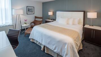 A hotel room with a large bed, a desk, a chair, a small table, and a floor lamp.