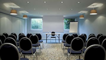 Un salón de conferencias con una pantalla para proyector, una pizarra y una mesa con sillas.