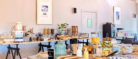 A breakfast buffet with various food items and beverages, a coffee machine, and a framed picture on the wall.