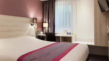 Una habitación de hotel con una cama grande, un escritorio, una silla, un televisor y un ventanal con cortinas.