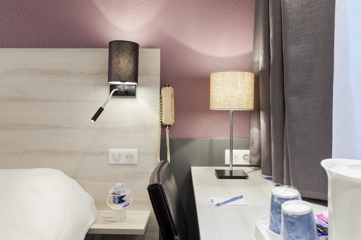 Habitación de hotel con una cama, un escritorio con lámpara, teléfono y una botella de agua.