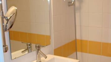 Un baño con lavamanos blanco, grifo cromado y ducha con cabezal cromado.