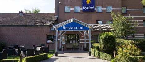 Egy szálloda, amelynek a bejárata a vendéglőhöz vezet, van kültéri ülőhelye, és „Kyriad Hotel” felirattal ellátott táblája található rajta.