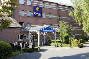A hotel with a restaurant sign, outdoor seating, and a well-maintained garden.