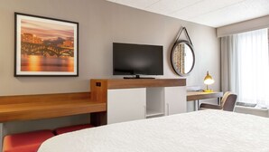 Une chambre d’hôtel avec un grand lit, un bureau avec un ordinateur, une télévision et un tableau encadré au mur.