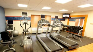 Une salle de sport équipée de tapis de course, de vélos elliptiques et d’un banc de développé couché.