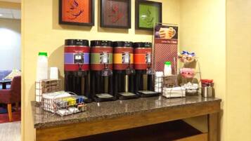 A coffee station with multiple coffee makers, a milk frother, and a sign indicating available food items.