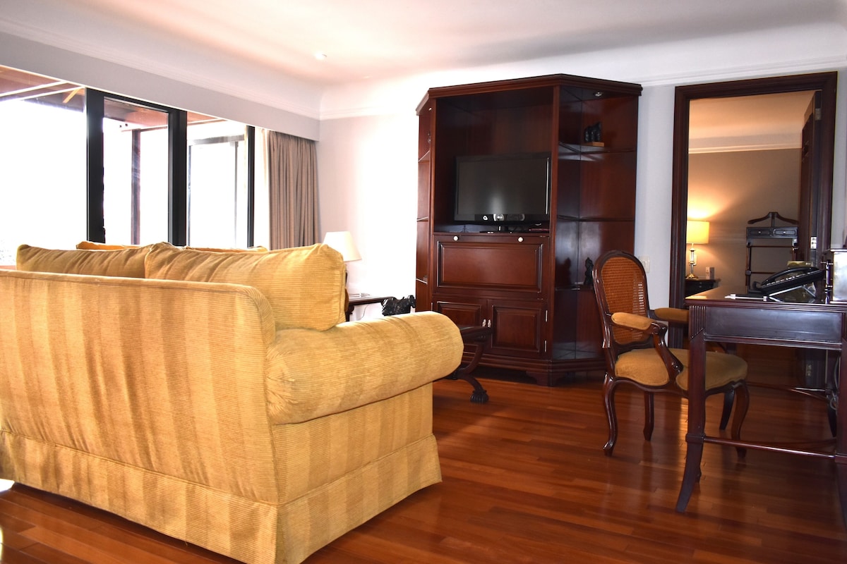 A hotel room with a sofa, a wooden cabinet, a television, and a desk.