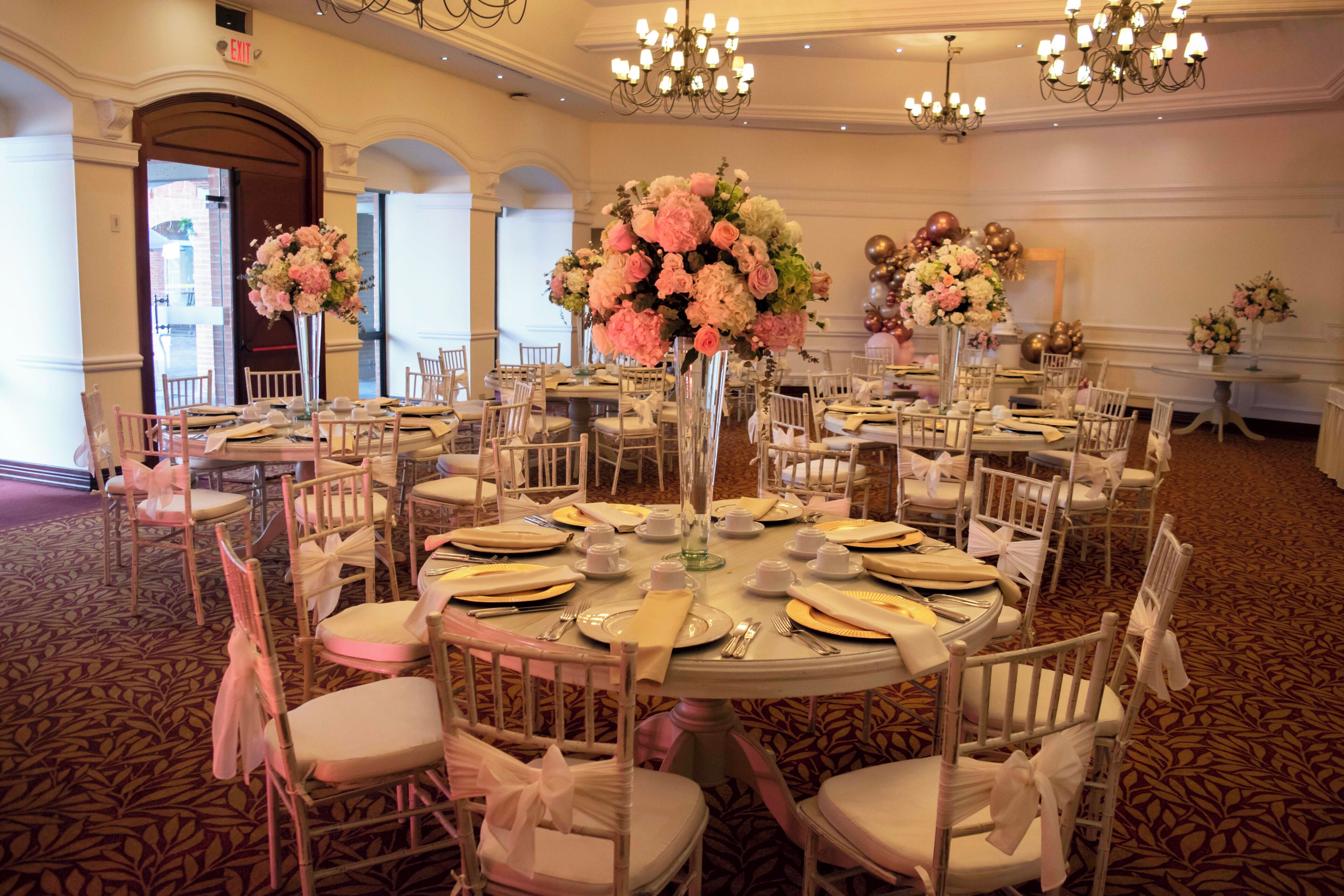 A banquet hall with round tables, white chairs, and floral centerpieces.