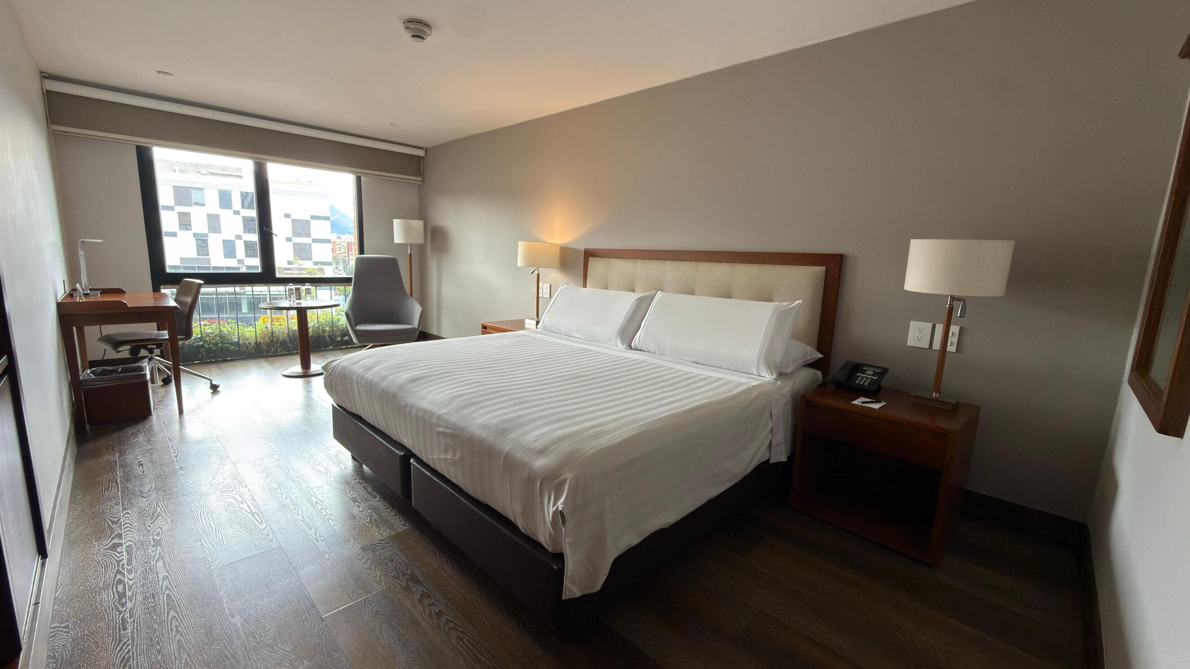 A hotel room with a large bed, a desk, a chair, and a balcony with a view.