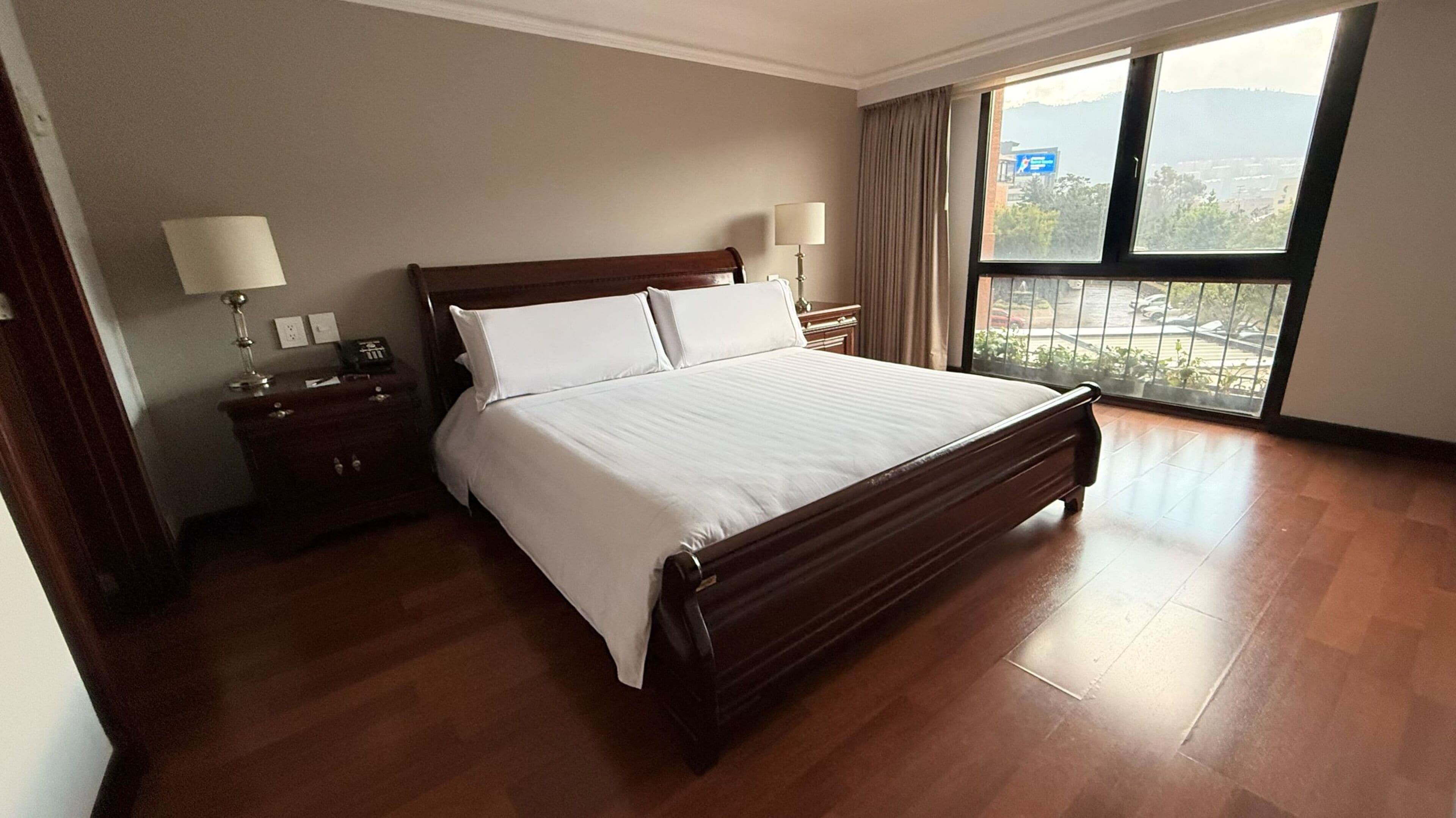 A hotel room with a large bed, bedside tables, lamps, and a view through a window.