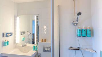 A bathroom with a sink, mirror, towel rack, and a shower area with a handheld showerhead and bottles of shampoo.