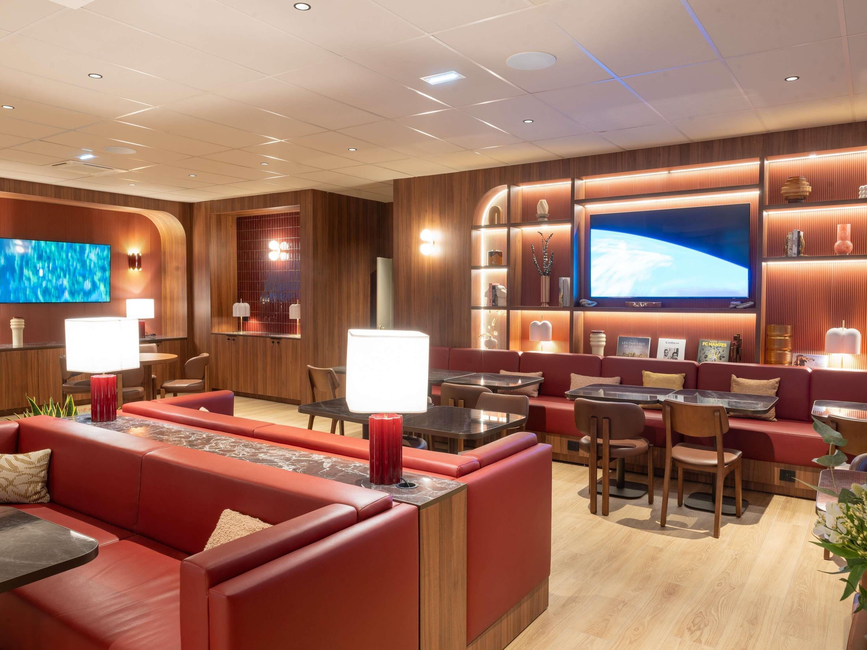 A modern lounge area with red sofas, wooden paneling, and a large flat-screen TV.