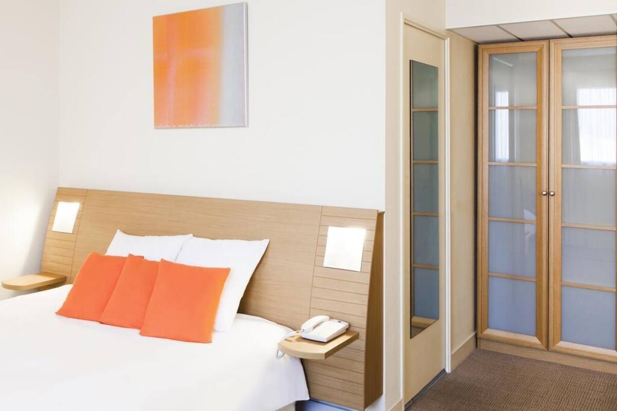 A hotel room with a bed, a bedside table with a phone, a wooden headboard, and a door with frosted glass panels.