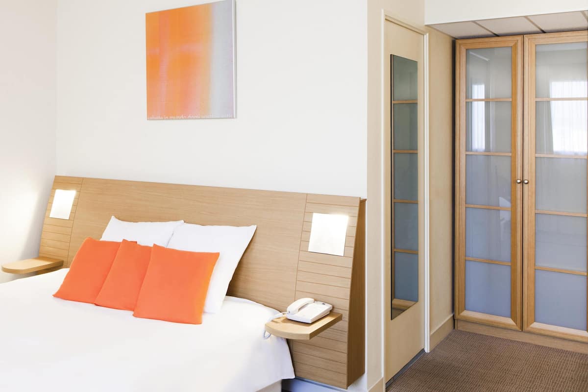 A hotel room with a bed, a bedside table with a phone, a nightstand, and a wardrobe with glass doors.
