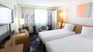 Habitación de hotel con dos camas, un escritorio con computadora, una silla, un televisor y una ventana con cortinas.