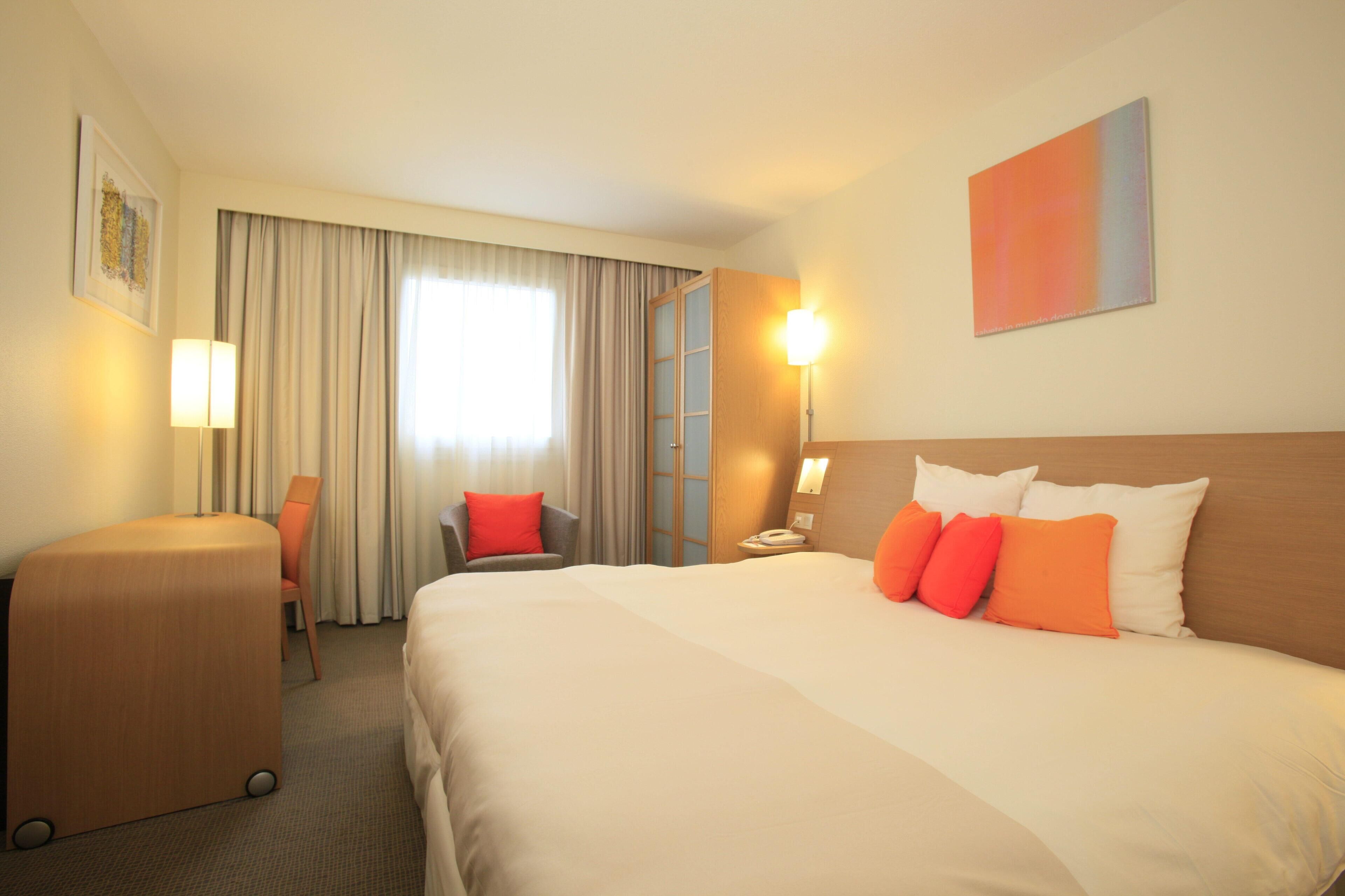 A hotel room with a large bed, a desk, a chair, and a window with curtains.